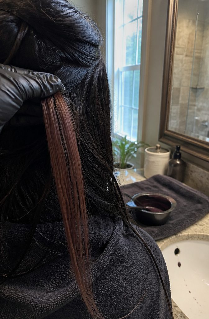 Black hair with a dyed strand beneath the lifted top layer and a gloved hand