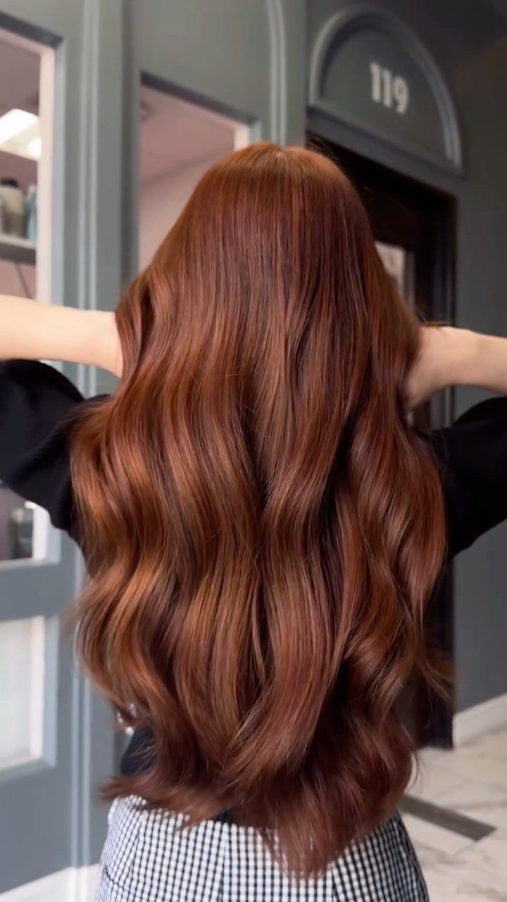 Long wavy auburn hair shown from behind in a salon