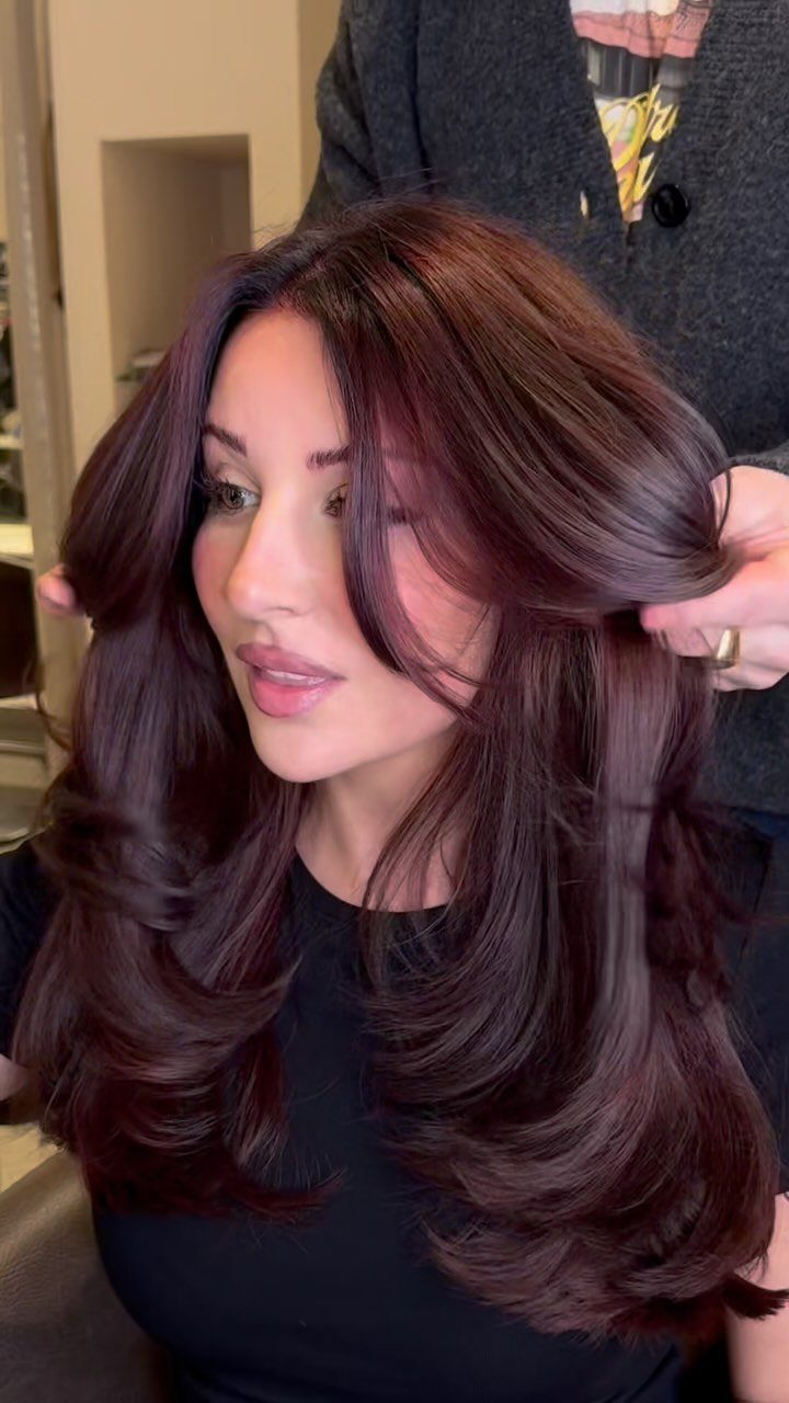 Woman showing long, glossy deep burgundy-red curls with layered volume