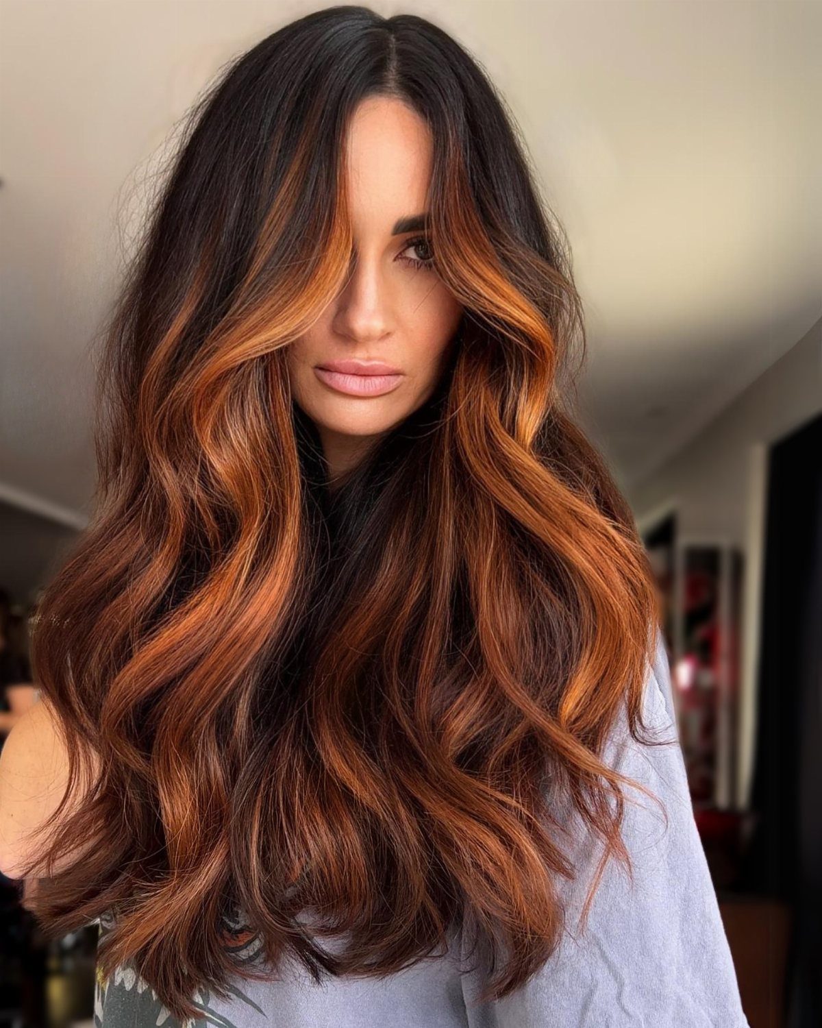Woman with long dark roots blending into wavy copper ombre hair