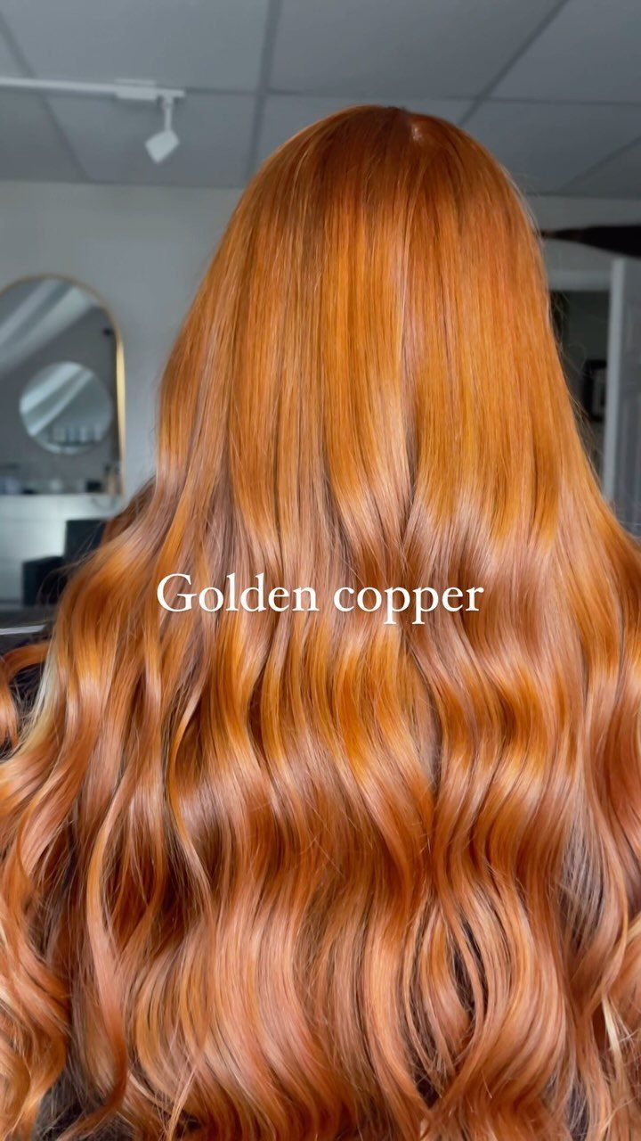 Long copper hair falls in glossy waves down a person's back in a salon.