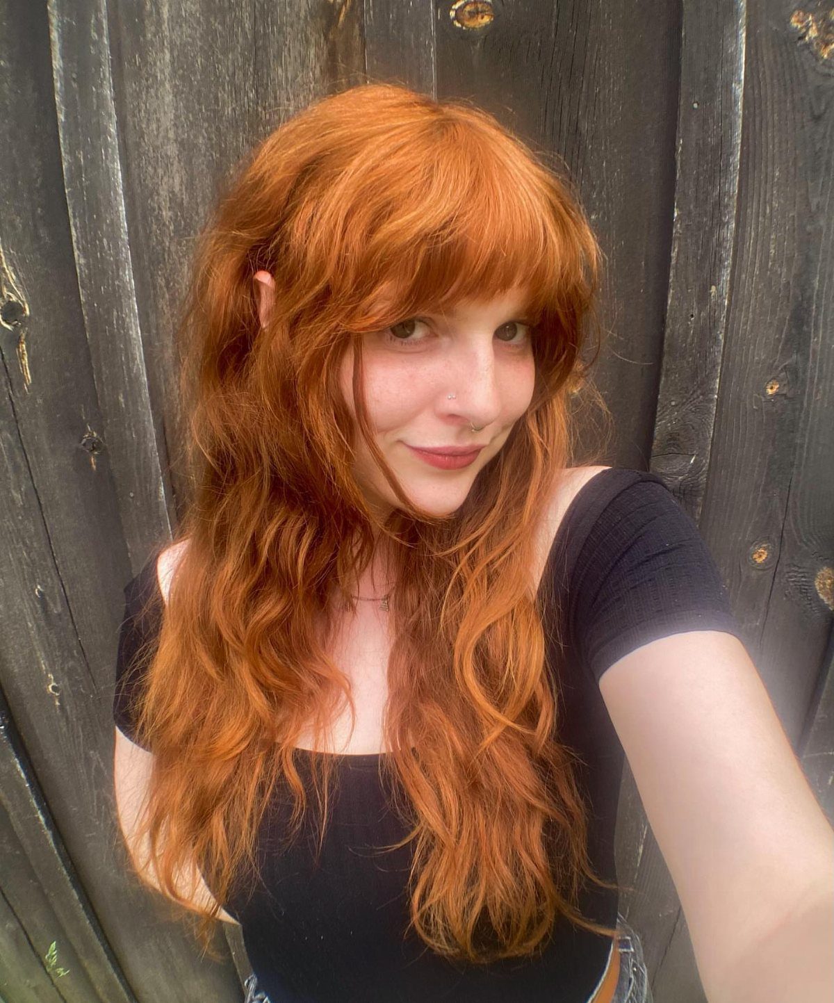 Woman with long, wavy copper ginger hair and a full fringe