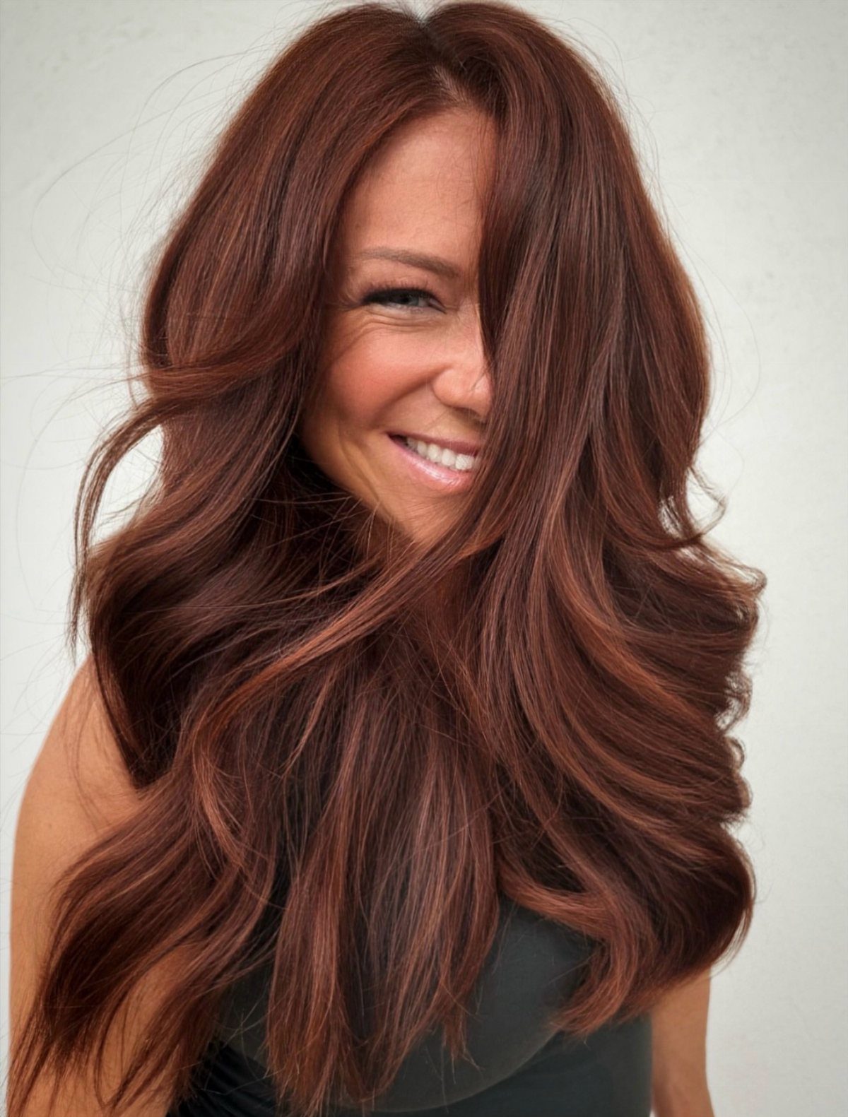 Woman showcasing long, wavy mahogany red-brown hair against a light background