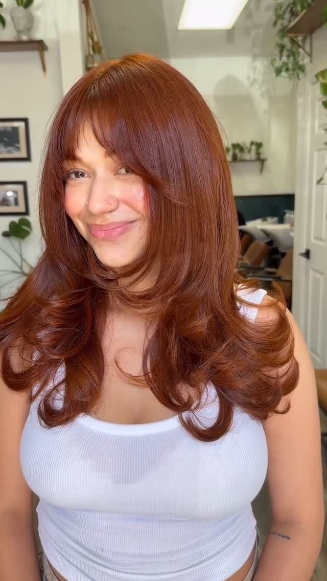 Woman posing in a salon with long, layered coppery reddish-brown hair