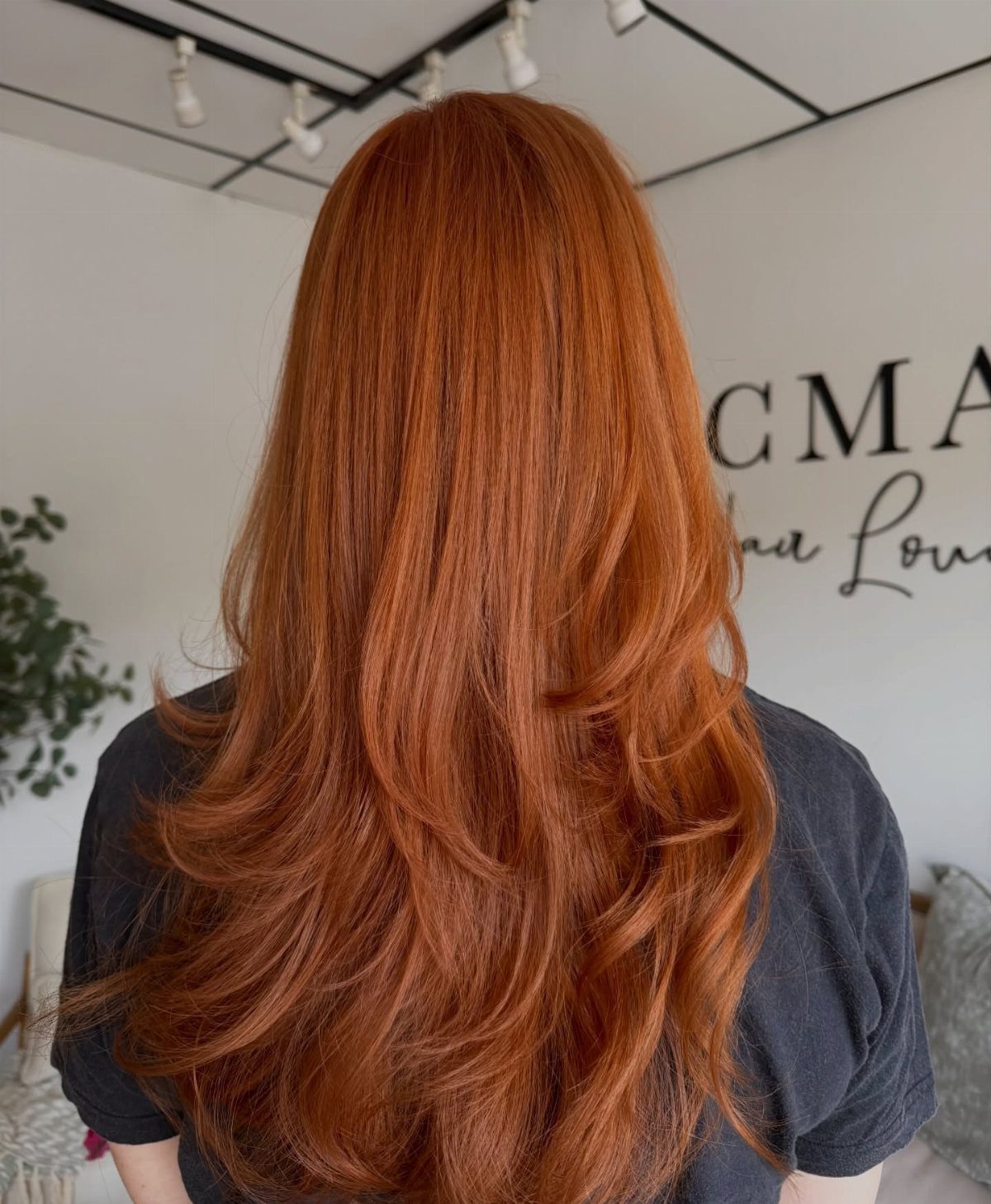 Long copper-red layered hair with curled ends shown from behind in a salon