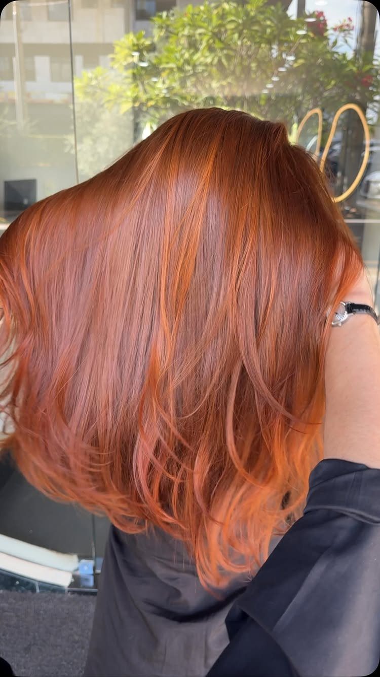 Glossy bright auburn hair falls in long, softly waved layers