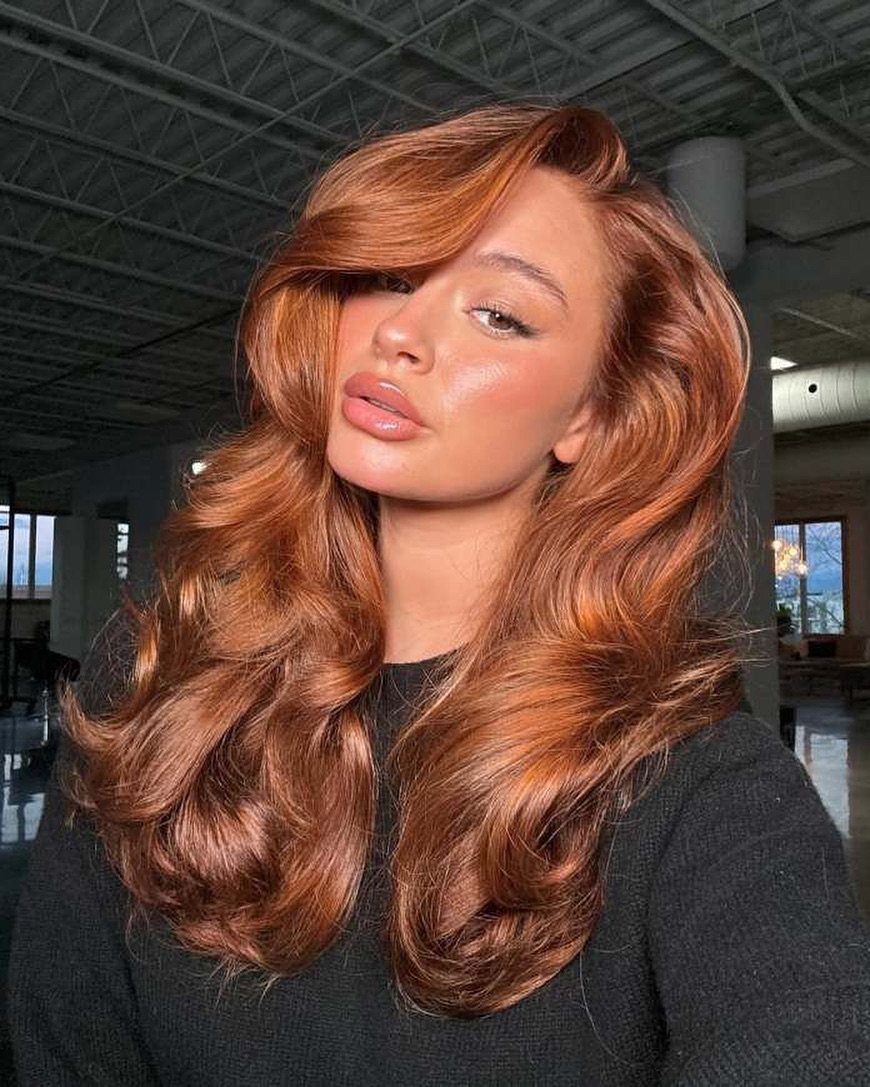 Woman displaying long copper waves with golden highlights in an industrial-style room