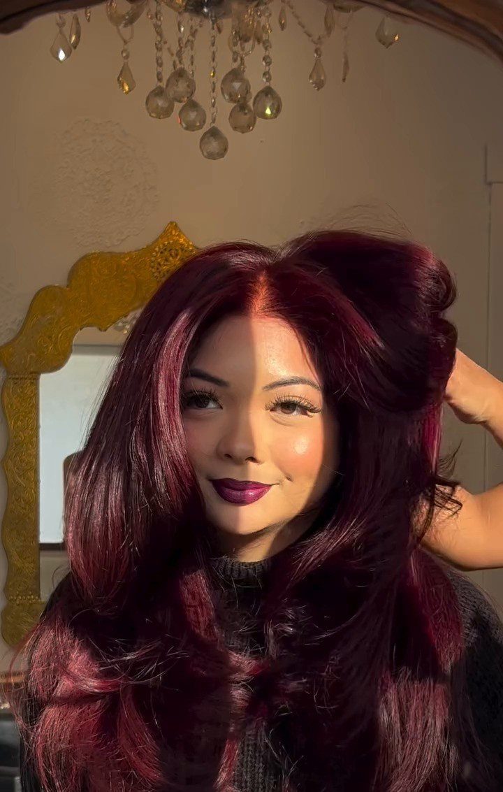 Woman with voluminous burgundy curls and a large styled updo posing indoors