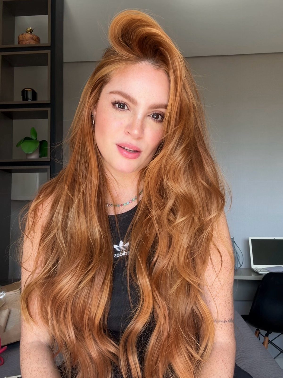 Woman with long wavy copper-red hair posing in a black sleeveless top