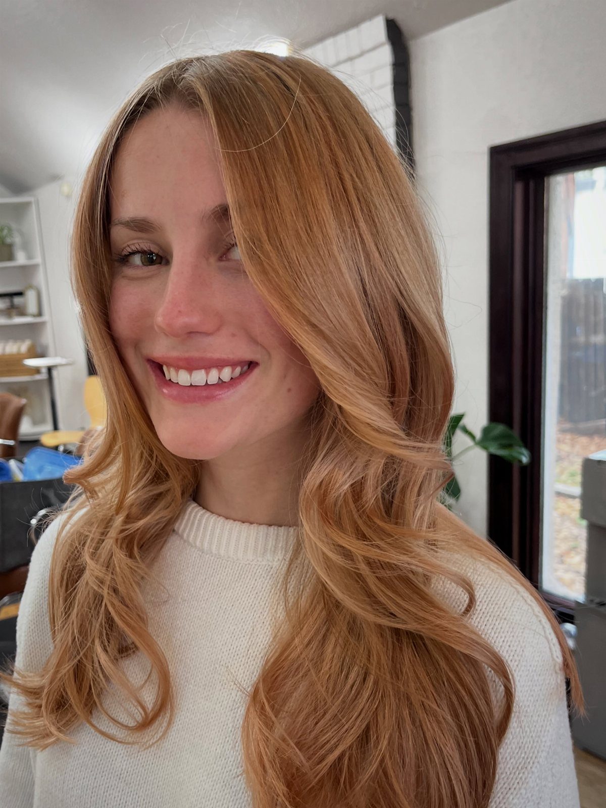Woman with long sun-kissed strawberry-blonde waves wearing a cream sweater