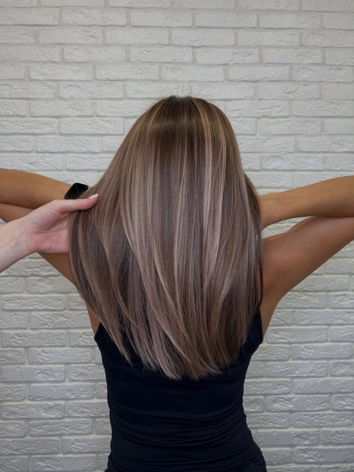 Long brown hair with fine, subtle lighter babylights against a white brick wall