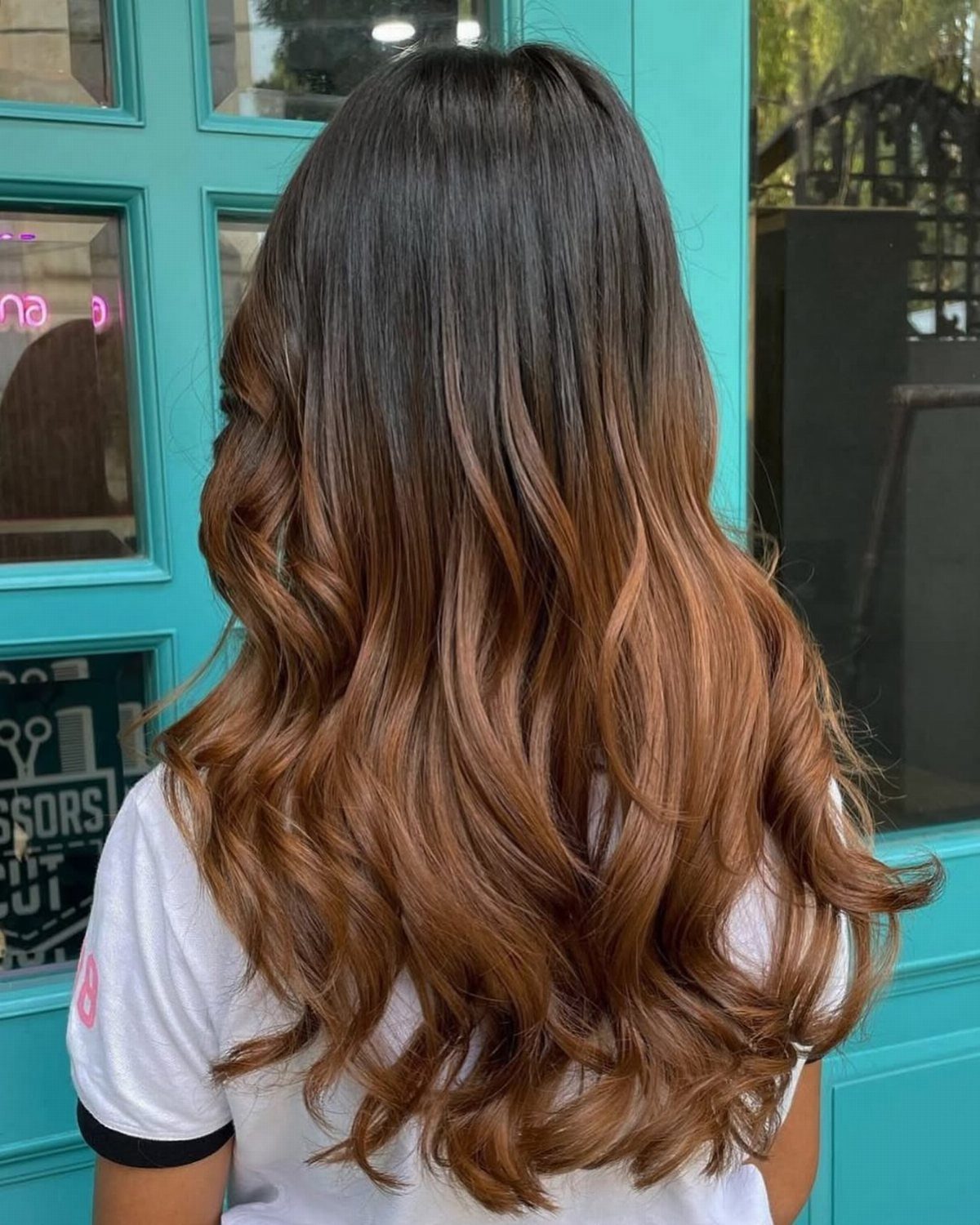Long wavy hair transitions from dark brown roots to honey-brown ends