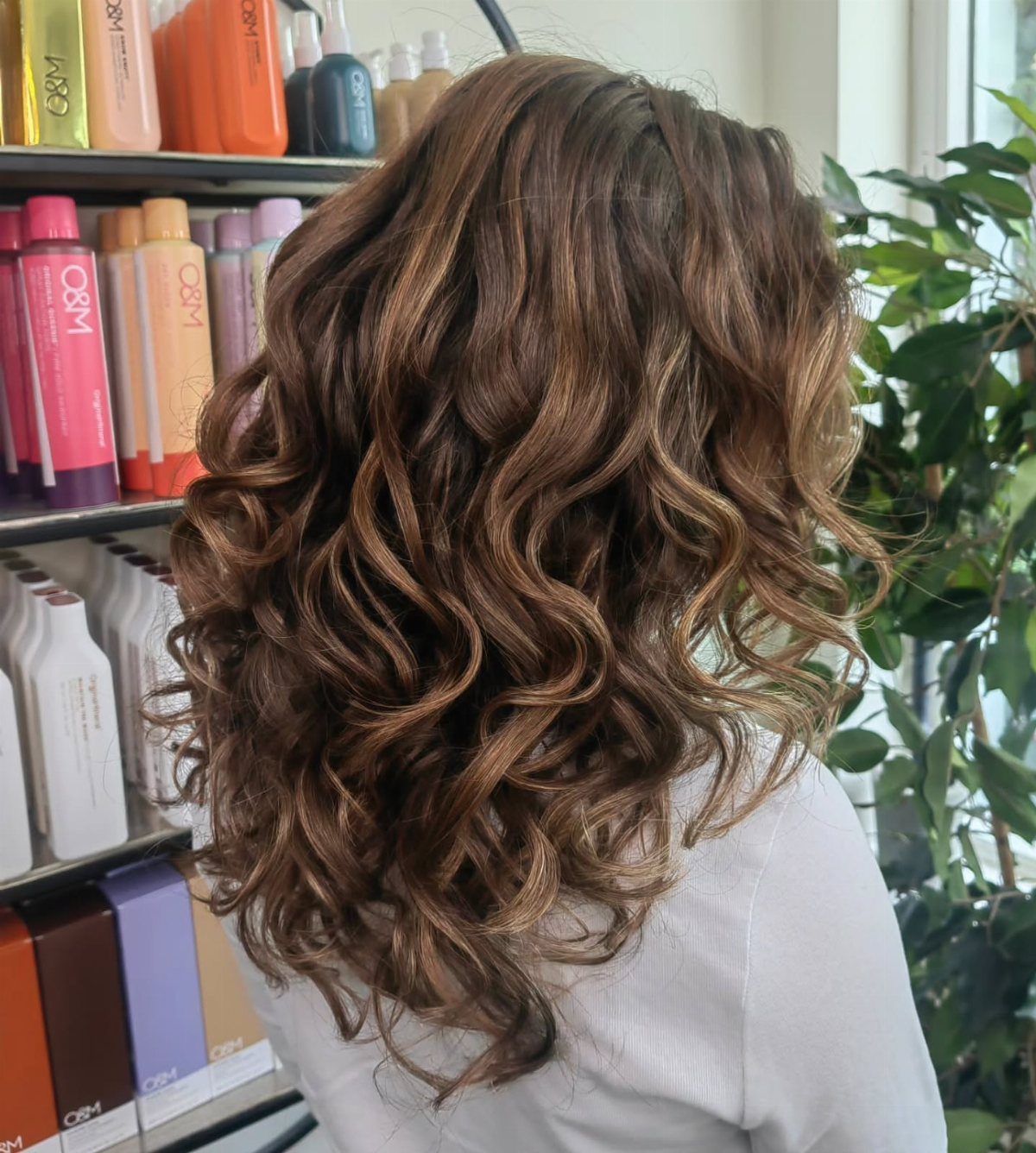 Layered brown curls with golden lowlights fall to the shoulders