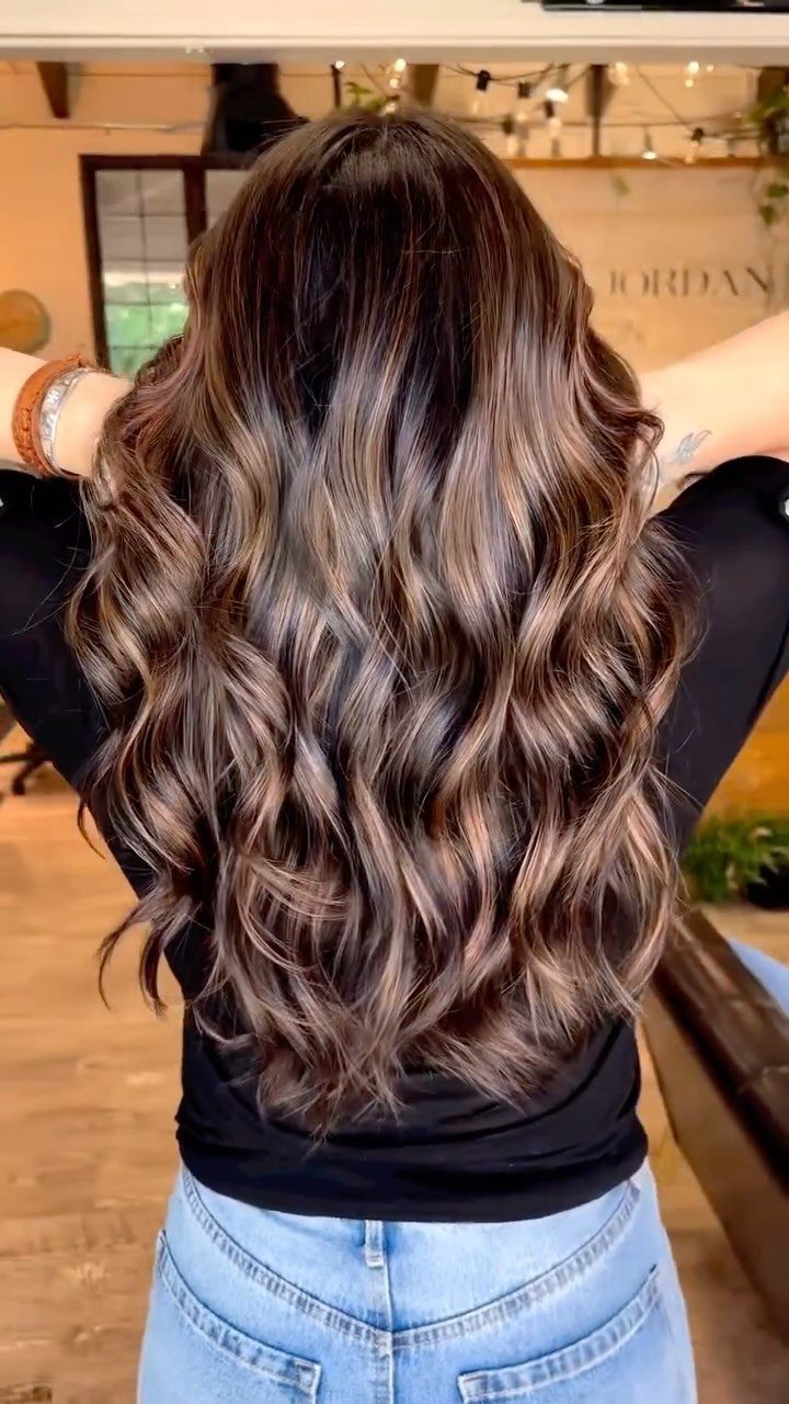 Long dark hair with warm caramel highlights styled in loose curls
