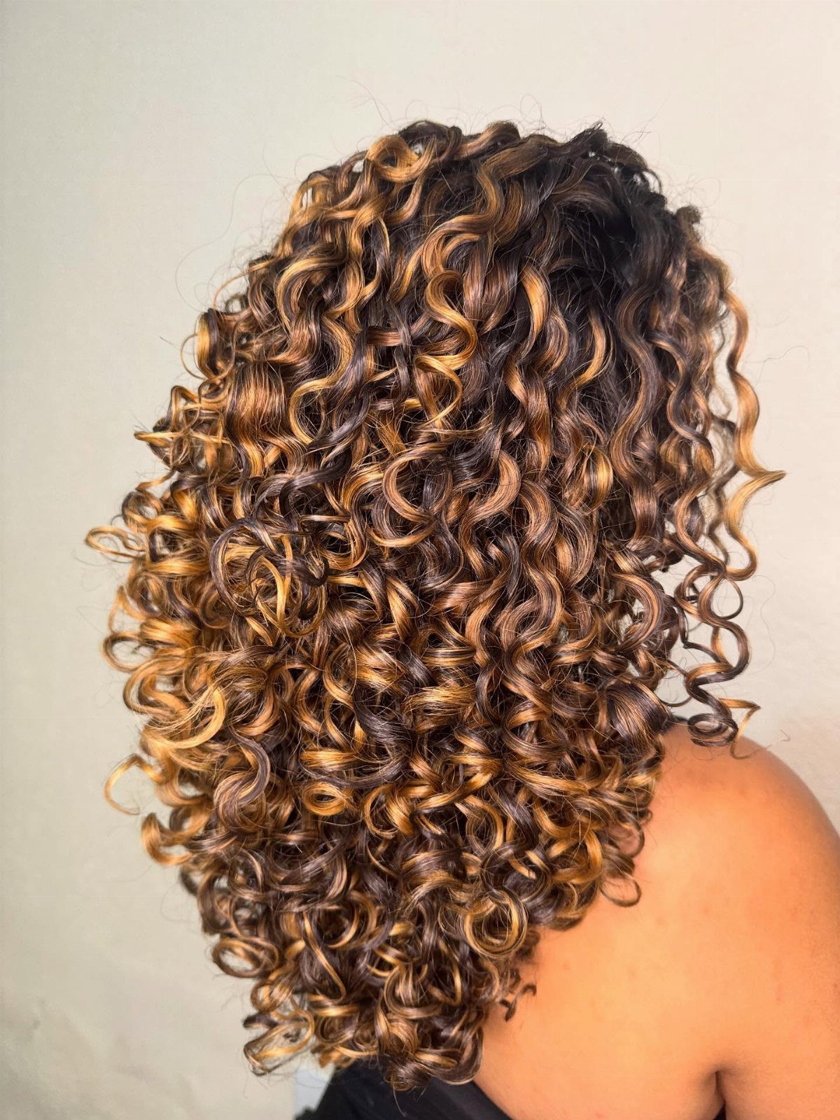 Dark springy curls show dimensional caramel highlights throughout