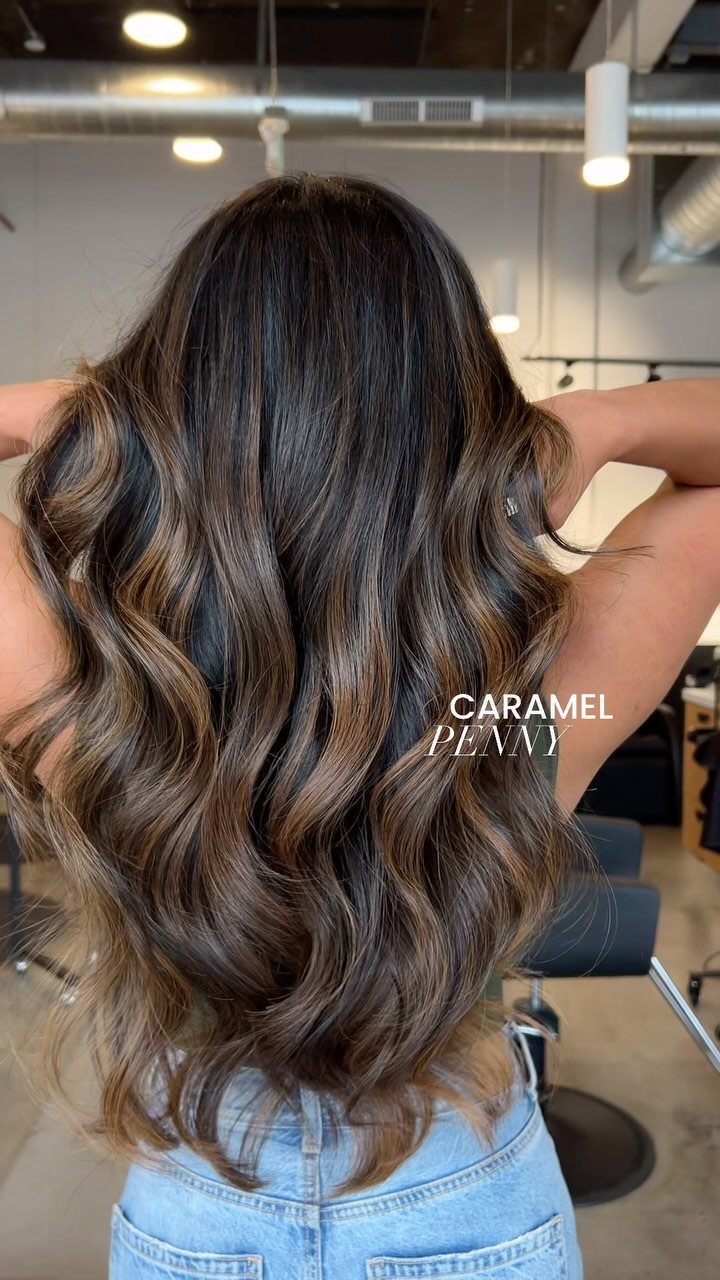 Long dark brown waves with caramel balayage highlights in a salon