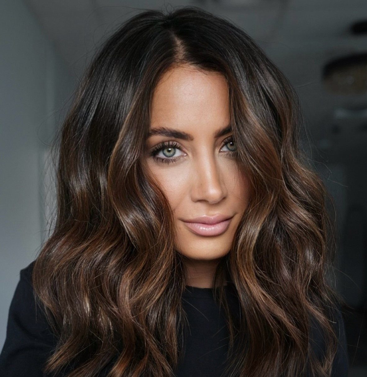 Woman showing wavy brunette hair with dark roots and caramel-brown blended lengths