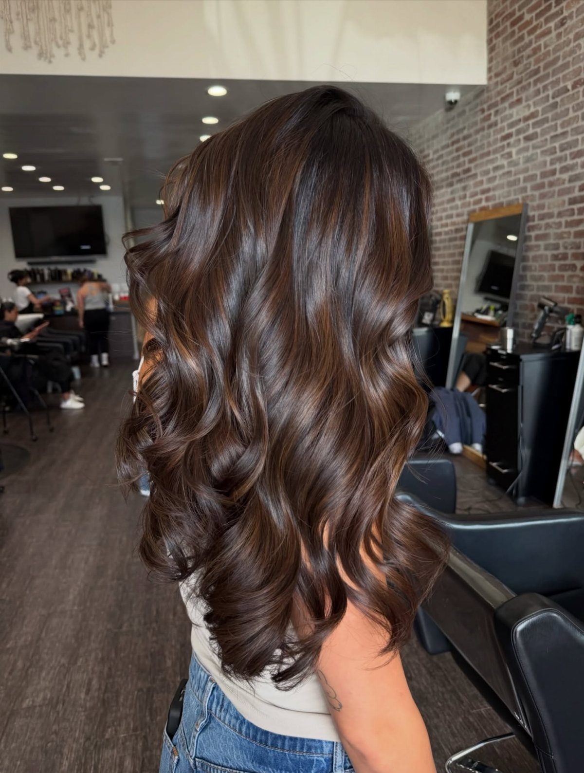 Loose dark brown waves show fine caramel streaks in a salon