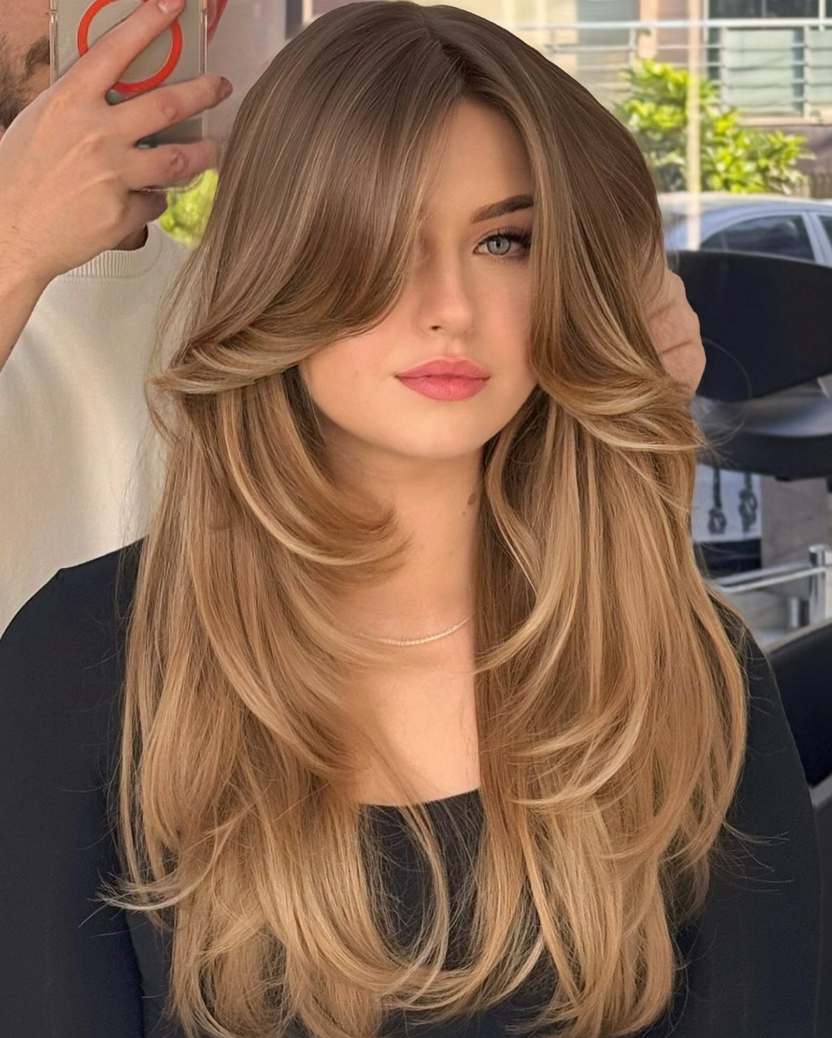 Woman displaying long, layered golden caramel hair with soft curtain bangs