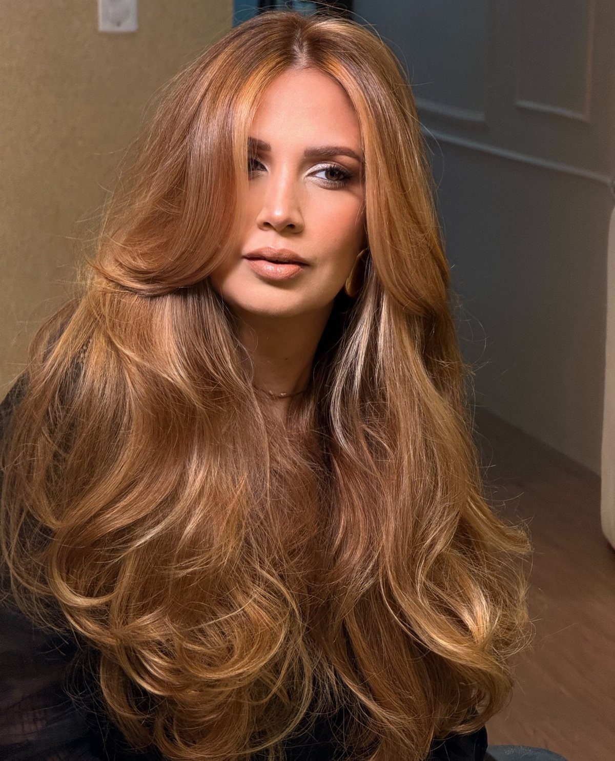 Woman with long, voluminous honey-caramel hair styled in soft curls