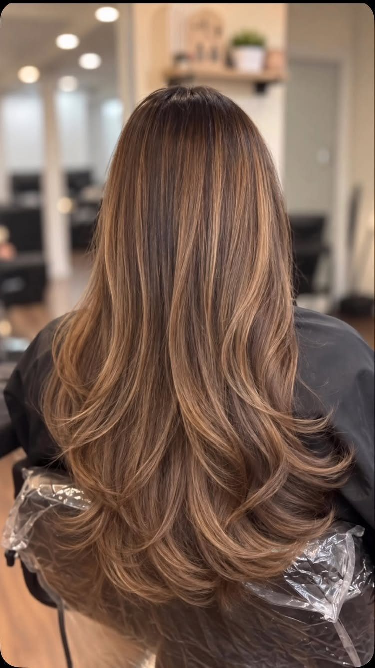 Long dark brown hair with delicate caramel ribbons and curled ends in a salon