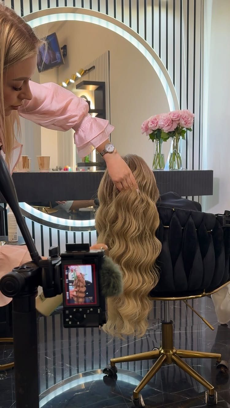 Stylist shapes long, fluffy blonde curls in a salon
