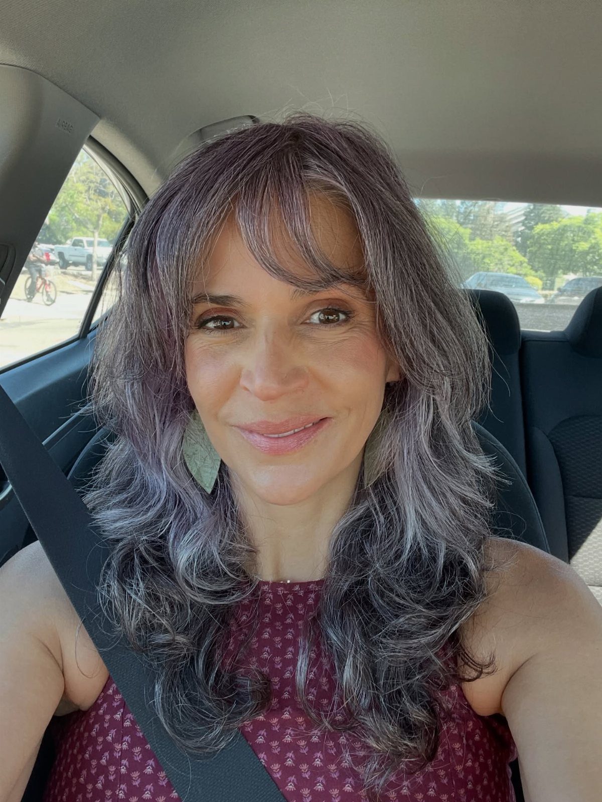 Woman with long, flowing dark layers and wispy bangs sitting in a car