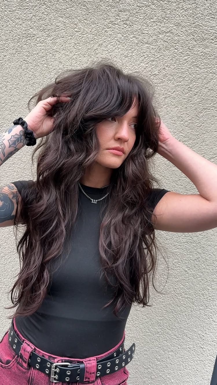 Woman poses with long layered dark waves, thick bangs, and a studded belt