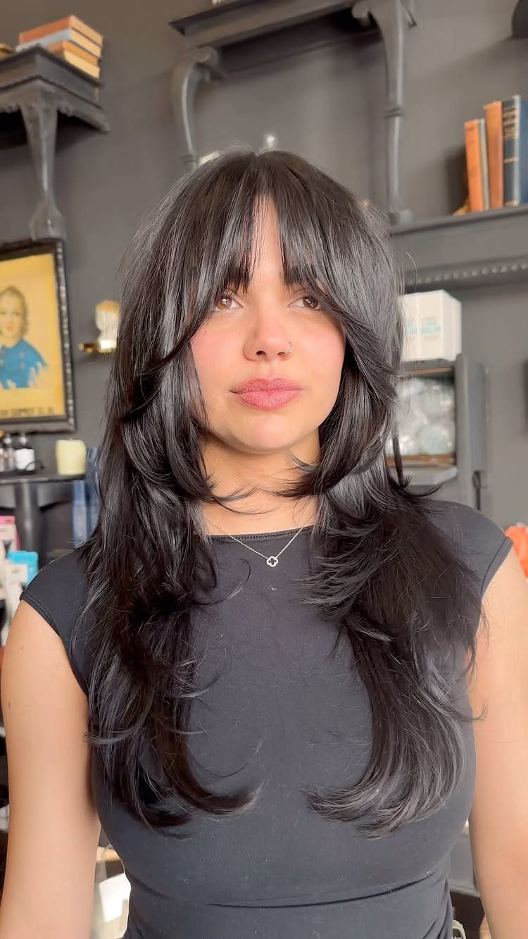 Woman with long dark hair styled in distinct, choppy layers and curtain bangs