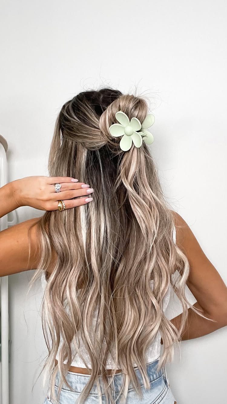 Long layered ash-blonde hair styled in soft waves with a white flower clip
