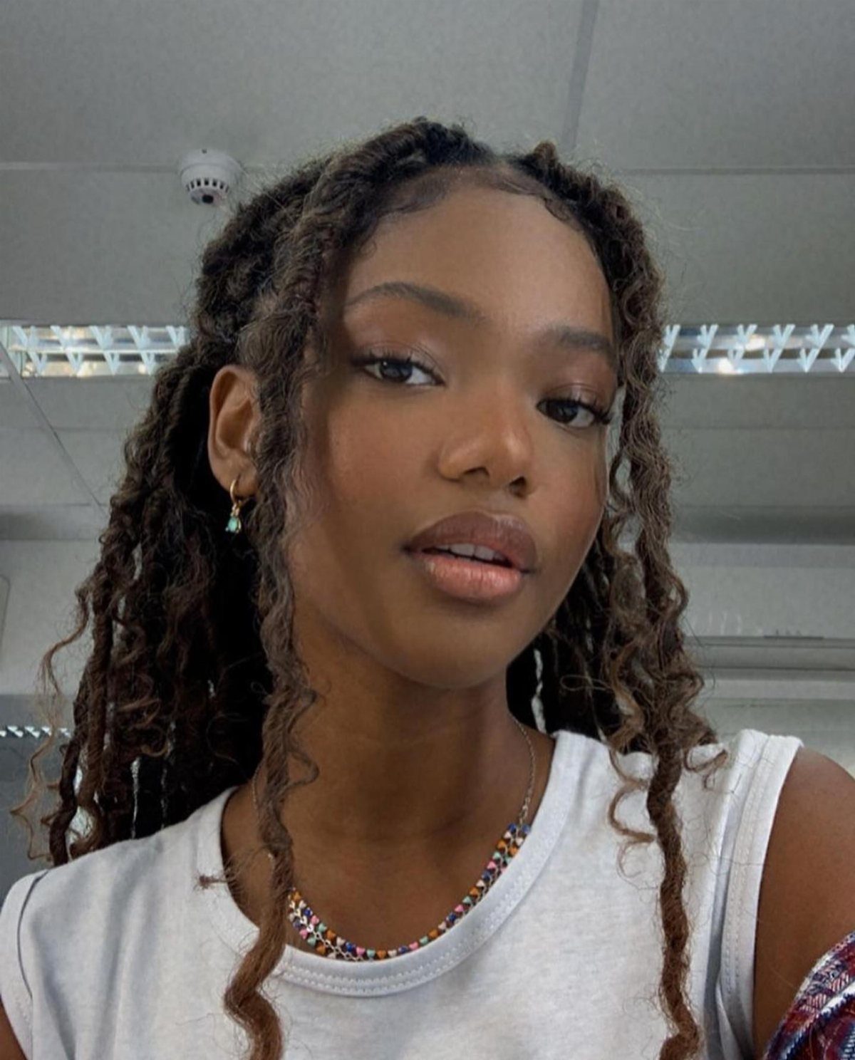 Woman with long dark brown-black curly locs wearing a white sleeveless top