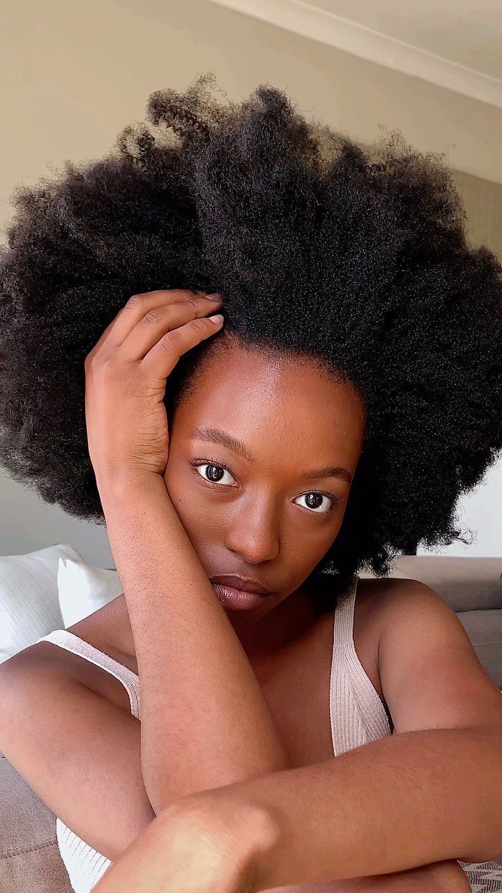 Woman with voluminous black afro-textured hair resting a hand against her head