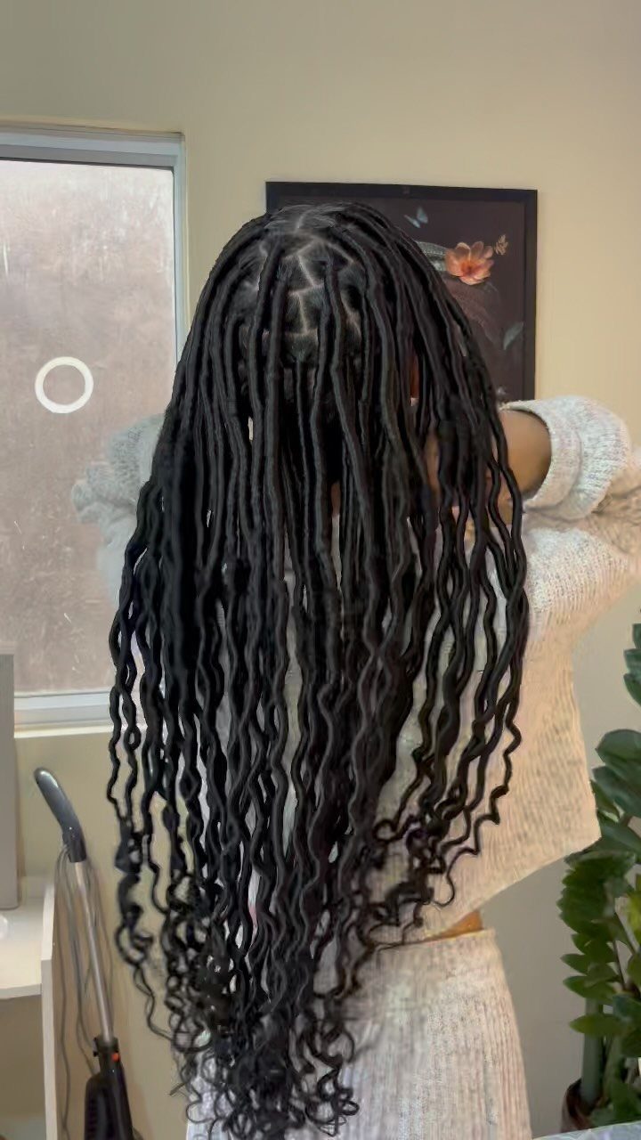 Long black faux locs cascade down the back with wavy curled ends