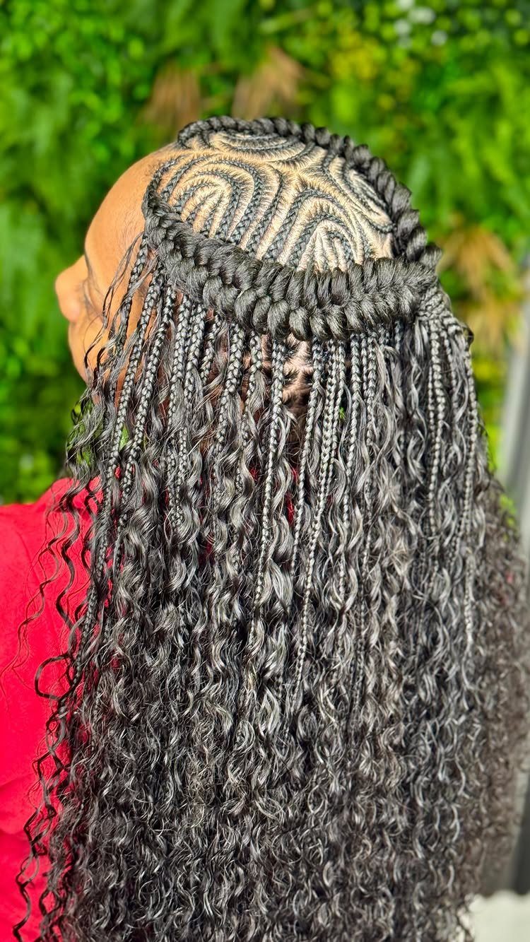 Long black braided hair with curved cornrows and curled extensions against green foliage
