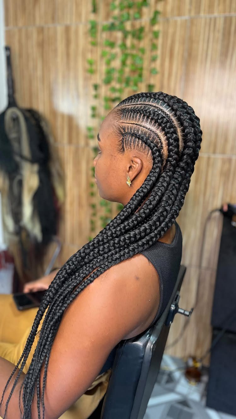 Long black Ghana braids extend from neat cornrows down a seated woman's back