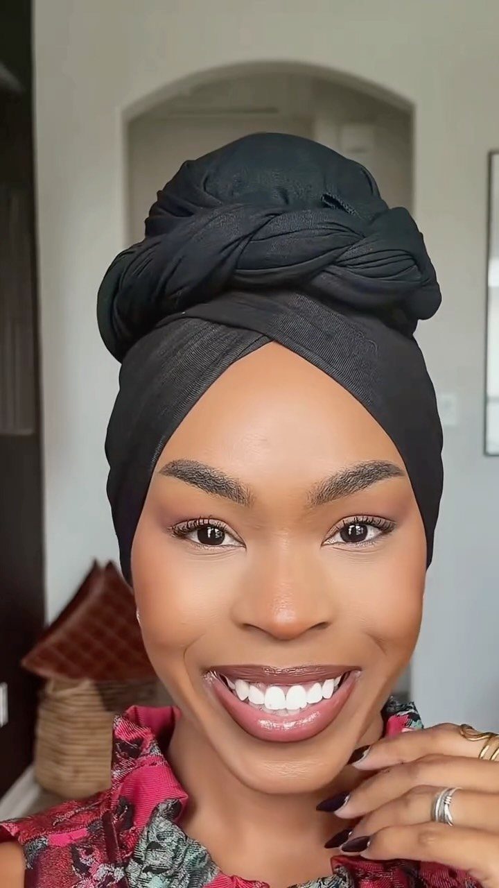 Woman smiling in a black twisted headwrap and patterned pink top