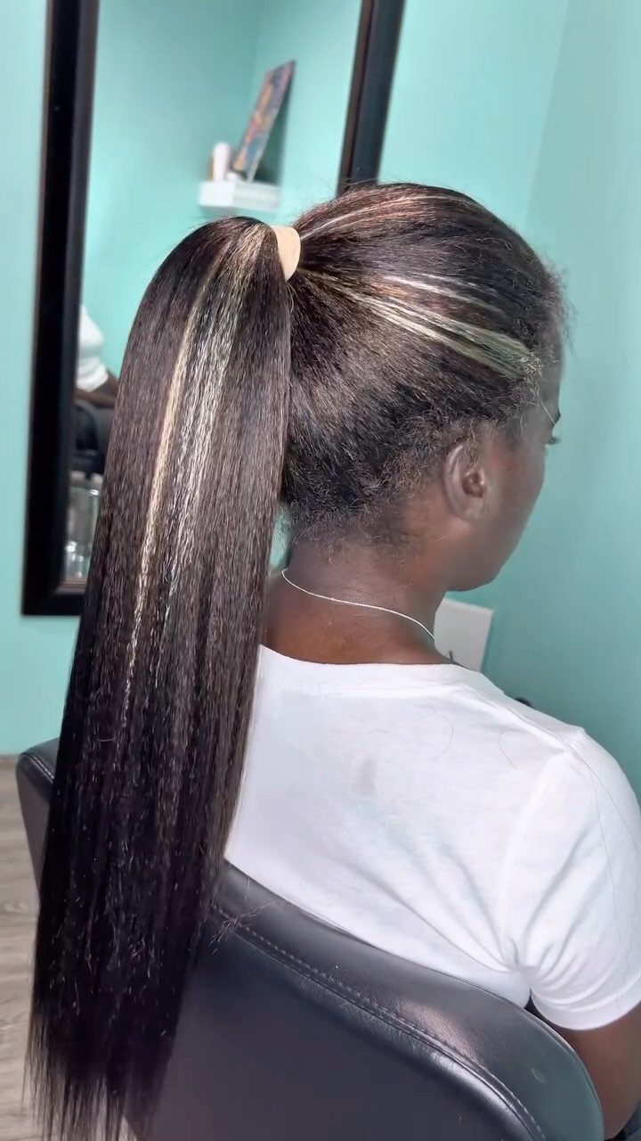 Sleek jet-black low ponytail with a defined side-swept part in a salon
