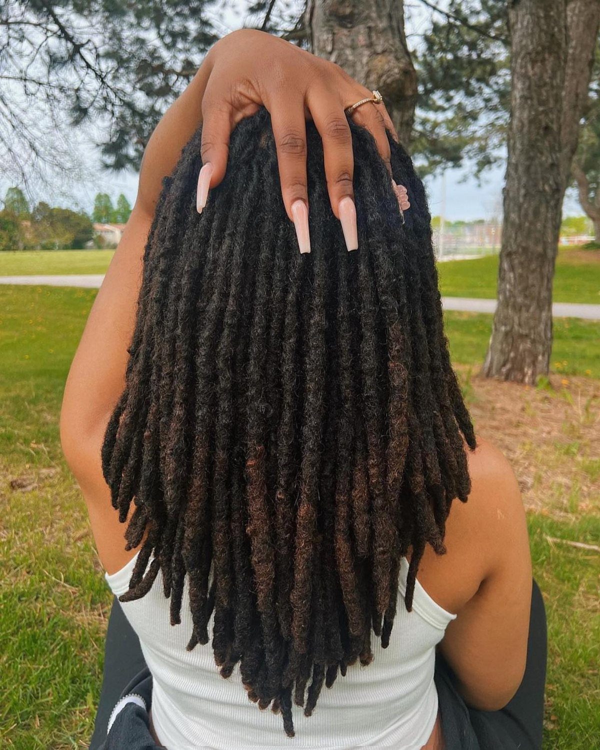 Long black locs fall down a person's back as one hand rests on their hair