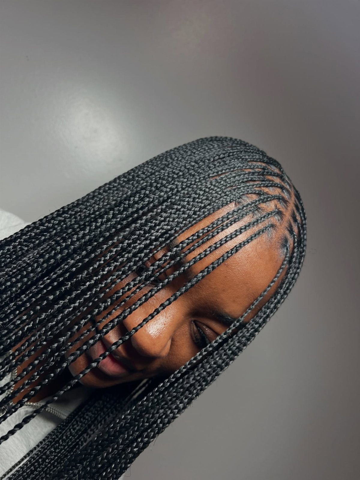 Long, tiny black braids frame a person's face against a gray wall
