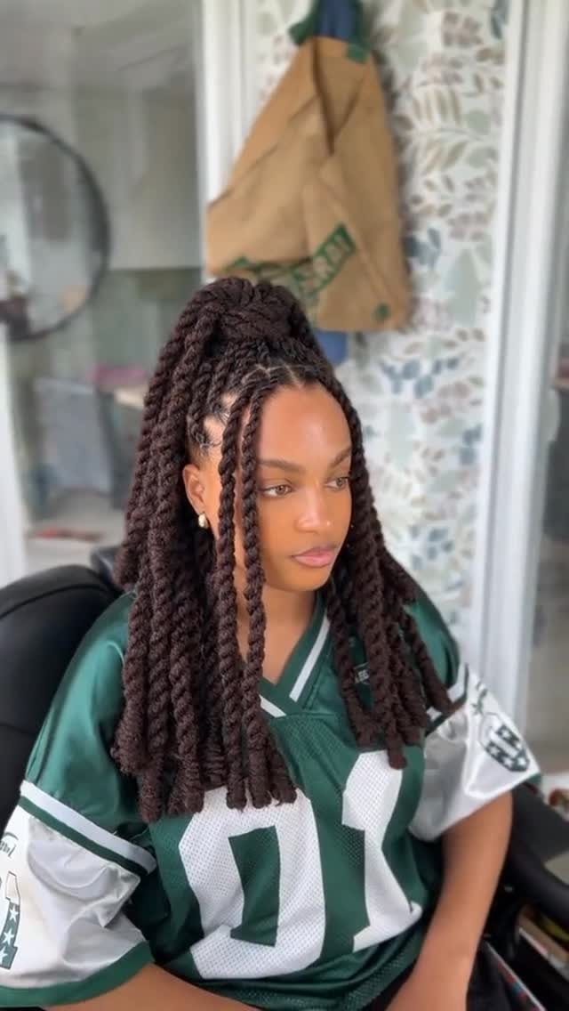 Long dark rope twists gathered high frame a woman wearing a green sports jersey