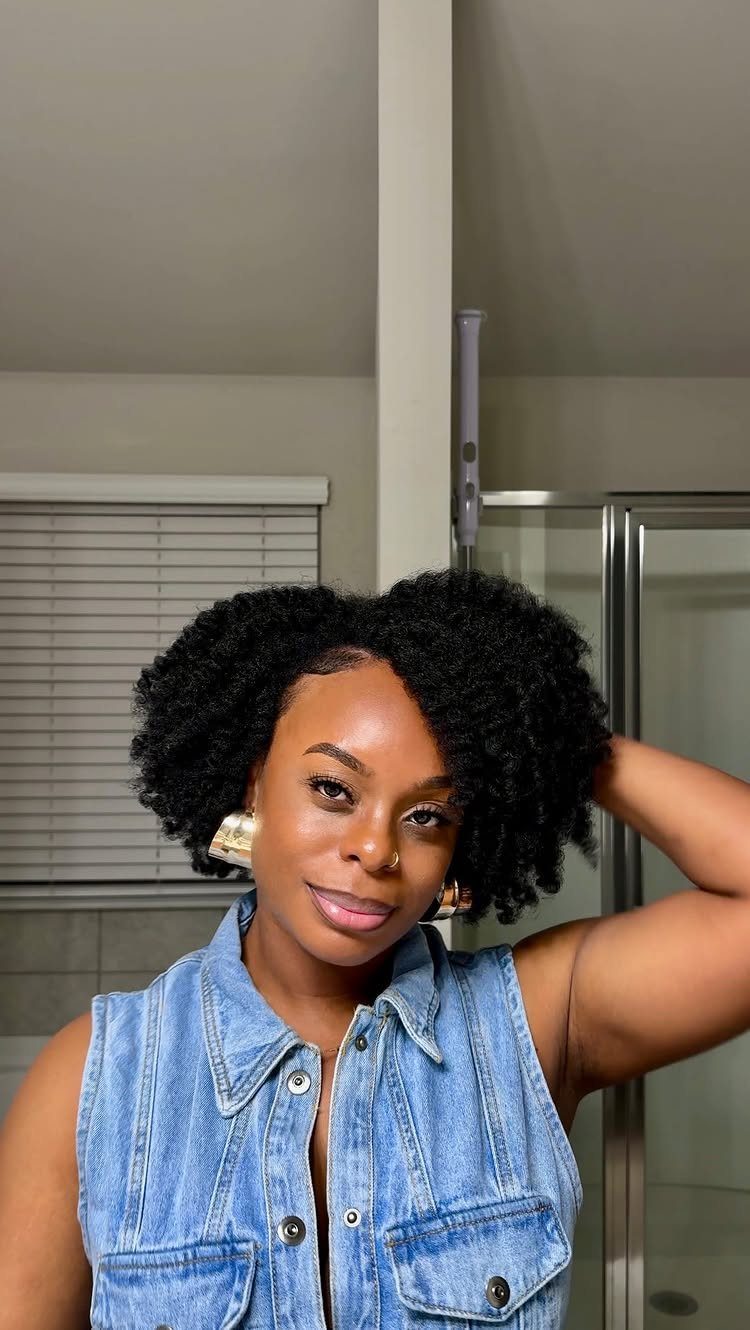 Woman poses with voluminous black textured hair and a sleeveless denim vest