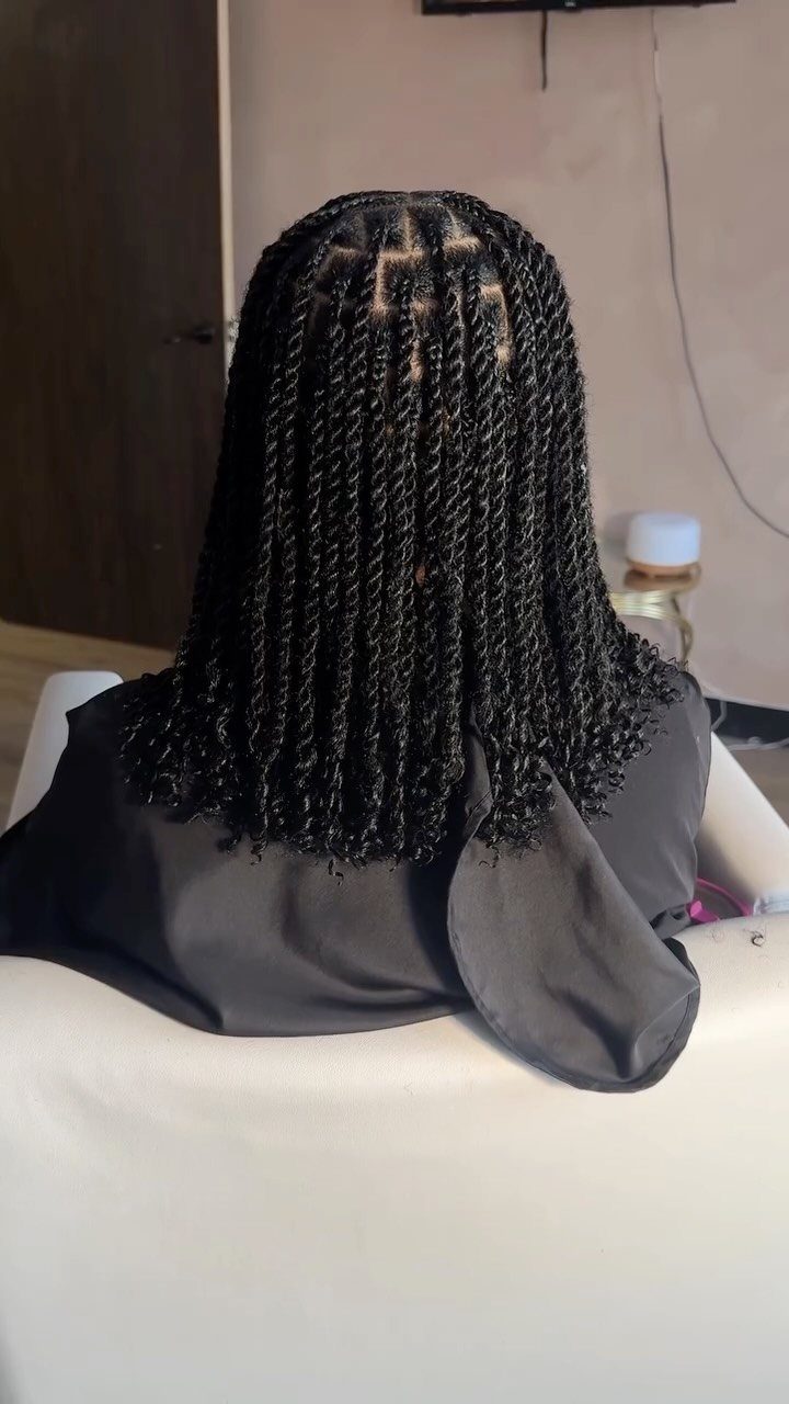 Black two-strand twists fall to the shoulders over a dark salon cape