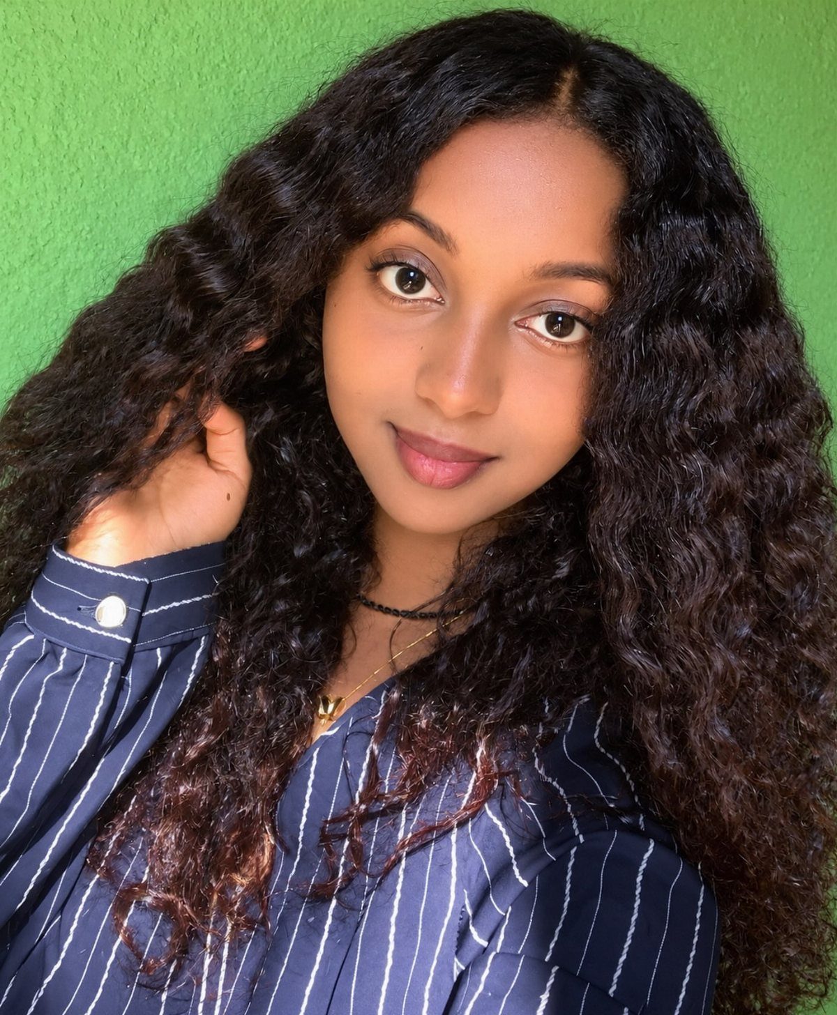 Woman posing with long, voluminous black curls against a bright green background