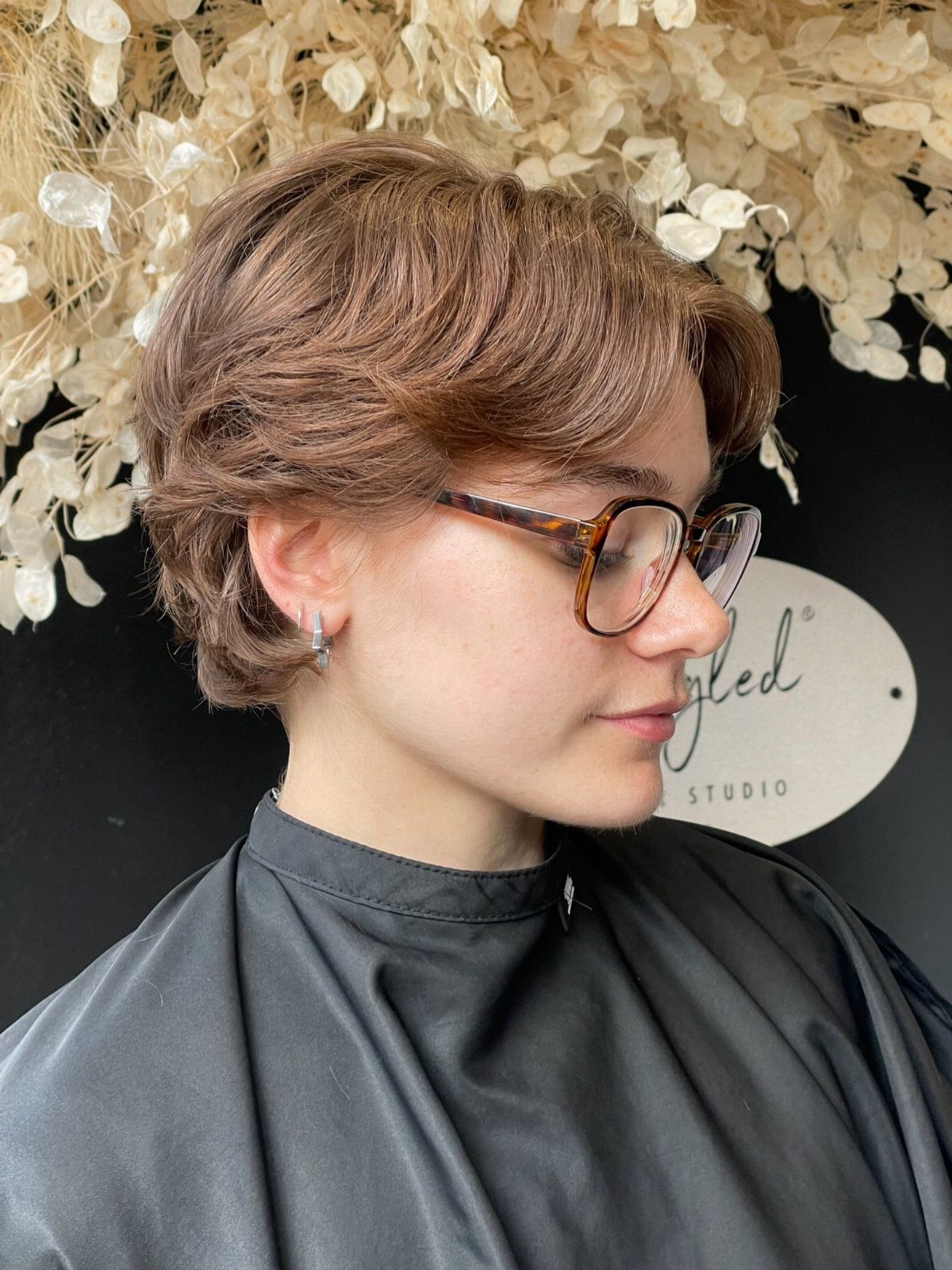 Short layered light-brown pixie with sweeping bangs, styled above the ears