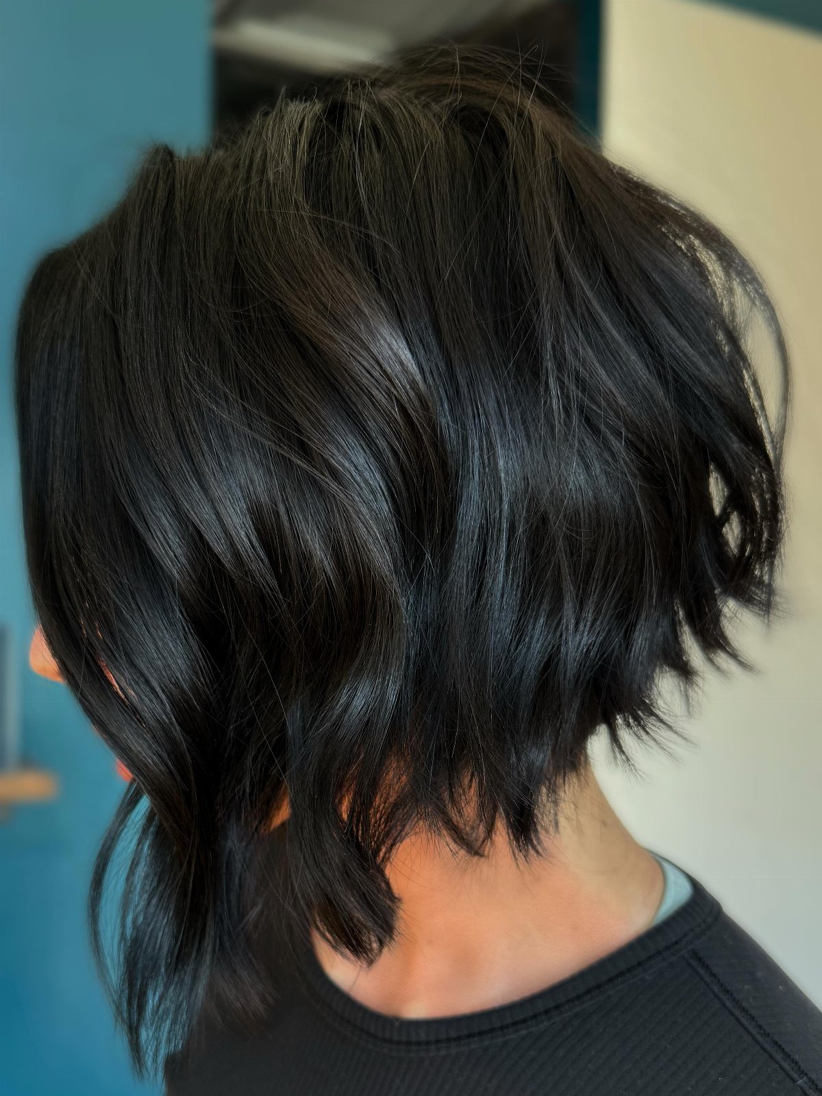 Short dark layered bob with tousled, wavy ends viewed from behind.