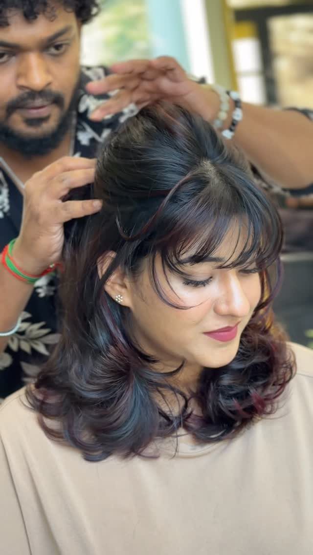 Woman with dark curled layers and bangs as a stylist shapes her hair