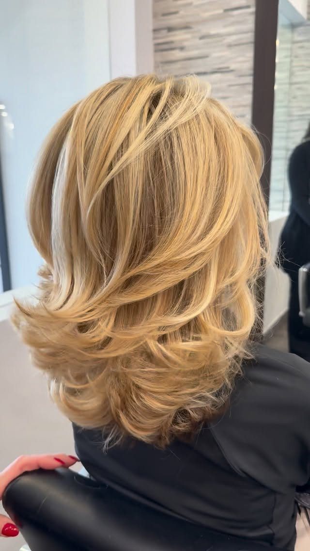 Medium-length blonde layered haircut with feathered waves and curled ends