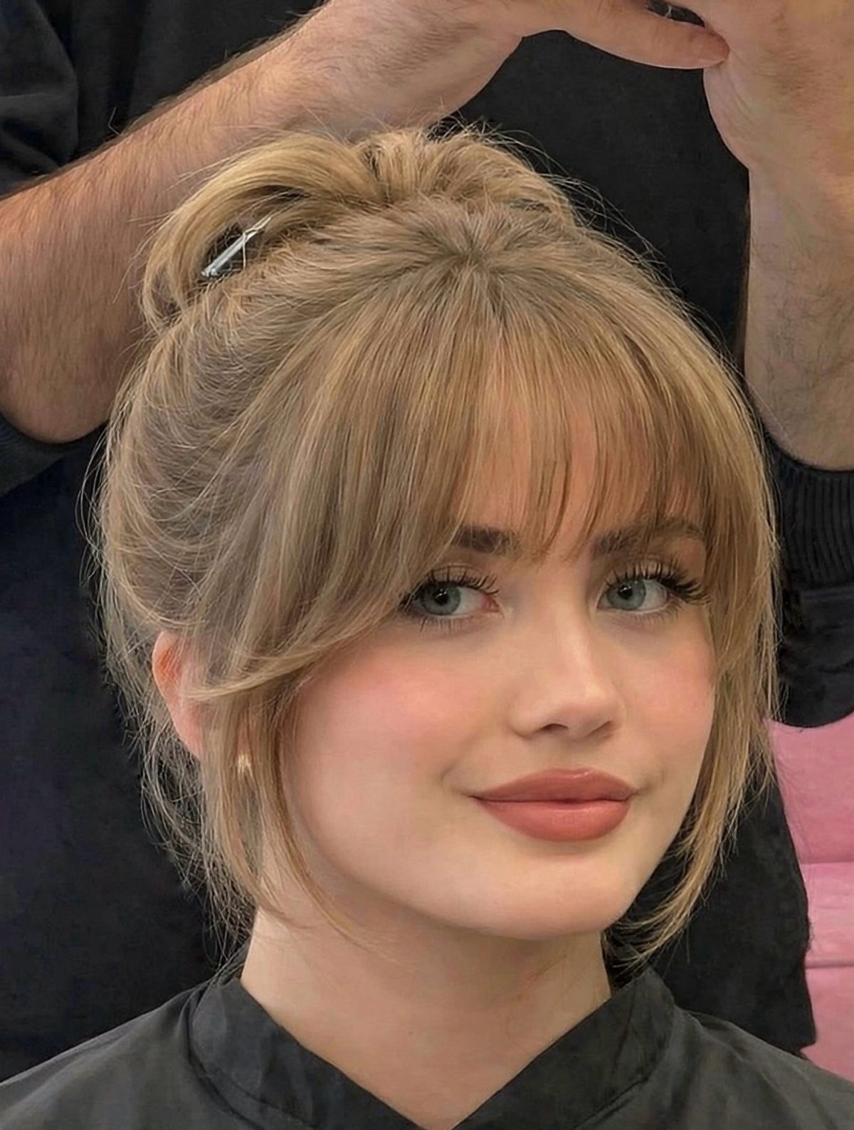 Blonde woman with a wispy see-through fringe and layered shoulder-length hair in a salon