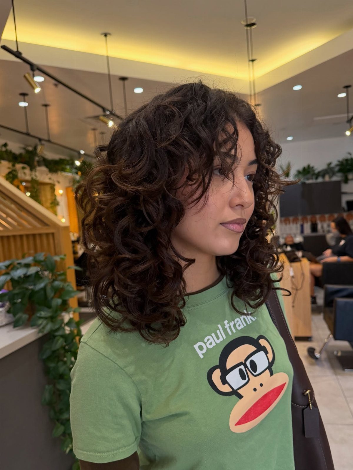 Woman with dark shoulder-length tight curls wearing a green graphic T-shirt