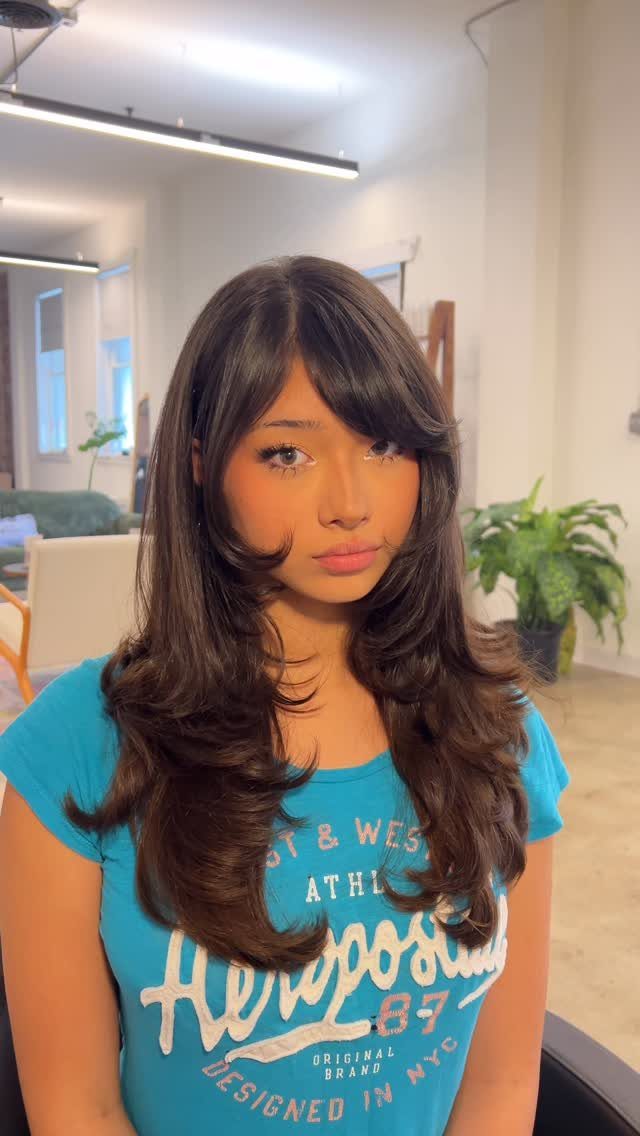 Woman with long, side-parted dark layered hair and softly curled ends